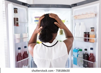 Rear View Of A Confused Young African Woman Looking In Open Refrigerator - Powered by Shutterstock