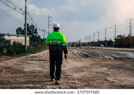 Rear view of construction supervisor walking along road construction site wearing safety helmet reflective uniform,representing infrastructure development,civil engineering management,transportation.