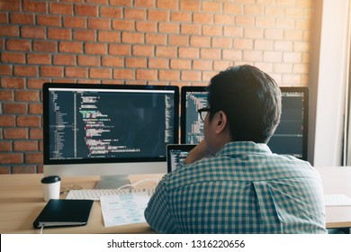 Rear view of contemporary website developer writing code for program and looking monitor screen with analyzing code.
