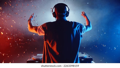 Rear view of cool dj performing in a nightclub, dancing at mixer controller and cheering the crowd up - nightlife concept  - Powered by Shutterstock