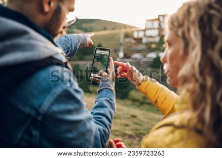 Rear view of a couple of hikers walking along mountain grassy trail and spending their time together in the nature while using maps to navigate with a smarthpone. Walking through pathway on mountain.