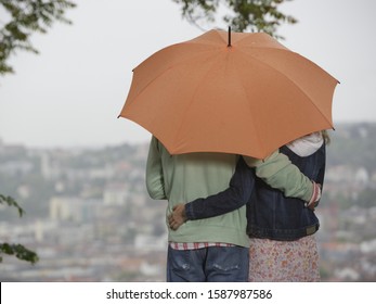 Rear View Of Couple Hugging Under Umbrella Outdoors