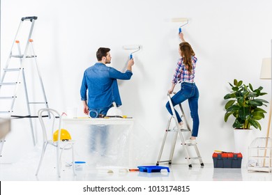 Rear View Of Couple Painting Wall With White Paint