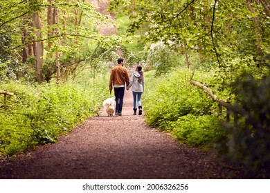 Rear View Of Couple With Pet Dog Walking Along Path Through Trees In Countryside