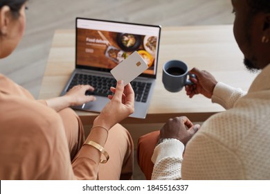 Rear View Of Couple Sitting In Front Of The Laptop And Using Credit Card For Online Shopping