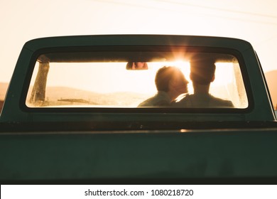 Rear view of couple sitting inside their pick up truck. Woman trying to kiss the man sitting inside the car. - Powered by Shutterstock