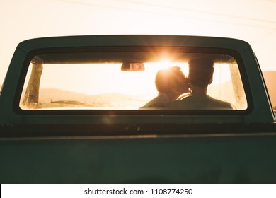 Rear View Of Couple Sitting Inside Their Pick Up Truck. Woman Kissing The Man Sitting Inside The Car.