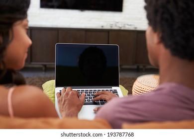 Rear View Of Couple Sitting On Sofa Using Laptop