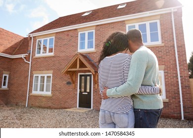 Rear View Of Couple Standing Outside New Home On Moving Day Looking At House