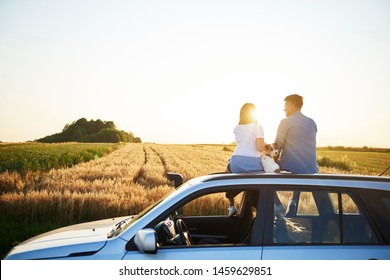 Rear View Of Couple And Their Dog Sitting On Car 