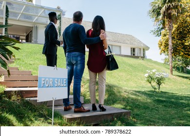 Rear View Of Couple Visiting Luxury Villa With Real Estate Agent. Property Broker Showing A House For Sale To Buyer Couple.