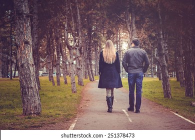 Rear View Of Couple Walking Through Autumn City Park