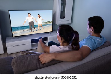 Rear View Of Couple Watching Movie On Television Together In Living Room