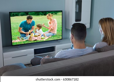 Rear View Of A Couple Watching Movie On Television At Home