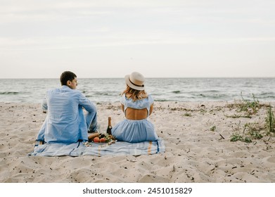 Rear view of couple while sitting on picnic blanket on sand sea. Female and male on beach ocean and enjoying sunny summer day. Man and woman having picnic date. spending time together. Back view - Powered by Shutterstock