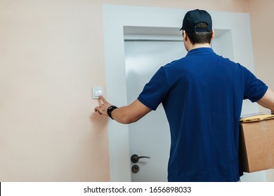 Rear View Of A Courier Carrying Packages And Ringing On Doorbell While Making Home Delivery. 