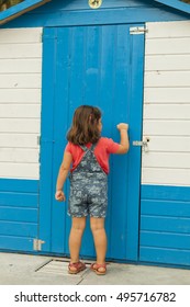 Rear View Curious Girl Knocking On A Striped Blue And White Door