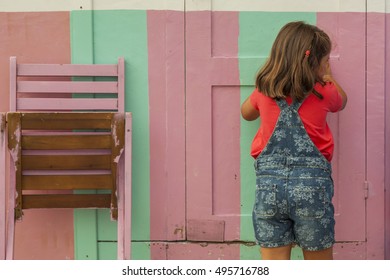 Rear View Curious Girl Knocking On A Striped Pink And Green Door