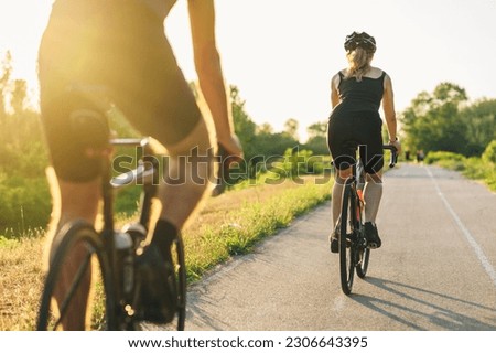 Rear view of a cycling woman and man riding on bikes outside of the city. Outdoor sport activity. Healthy lifestyle. Attractive young couple cycling together on their high performance bikes.