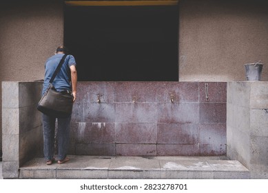 Rear view of a devotee standing at the ablution tap area performing ritual washing before entering Sri Maha Mariamman Temple in Kuala Lumpur.