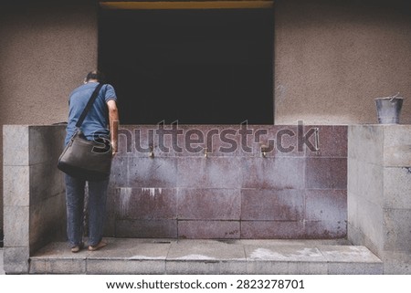 Rear view of a devotee standing at the ablution tap area performing ritual washing before entering Sri Maha Mariamman Temple in Kuala Lumpur.