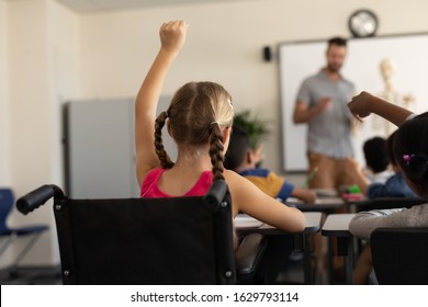 Rear view of disable schoolgirl raising hand in classroom of elementary school - Powered by Shutterstock