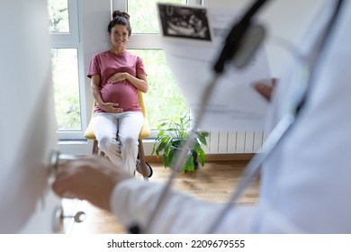 Rear View Of Doctor Calling Pregnant Woman In Waiting Room For Appointment