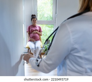 Rear View Of Doctor Calling Pregnant Woman In Waiting Room For Appointment