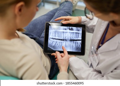 Rear View Of Doctor Showing X-ray Of Teeth On Digital Tablet To The Patient At Dental Clinic