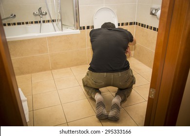Rear View of a Drunk Young Man Vomiting in the Toilet at Home While in Kneeling Position.