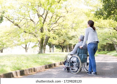 Rear View Of Elderly Man In Wheelchair And Care Helper