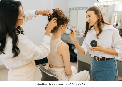 Rear view of elegance curly young woman getting professional makeup from make up artist in beauty studio. Hairstylist doing stylish hairdo to long haired female. Beauty and hair styling concept - Powered by Shutterstock