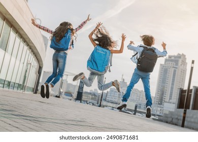 Rear view of energetic elementary middle school kids children pupils classmates friends boys and girls with backpack in casual clothes jumping and having fun together at school yard