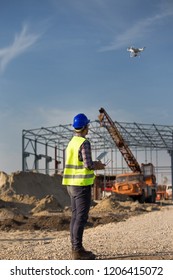 Rear view of engineer controlling drone above building site with metal construction and crane in background