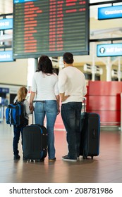 Rear View Of Family Checking Flight Information At Airport