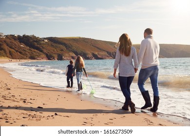 Rear View Of Family With Fishing Nets Walking Along Shoreline Of Winter Beach