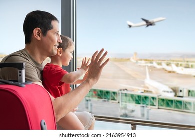 Rear View Of A Family Looking And Waving Through The Window To A Plane In An Airport