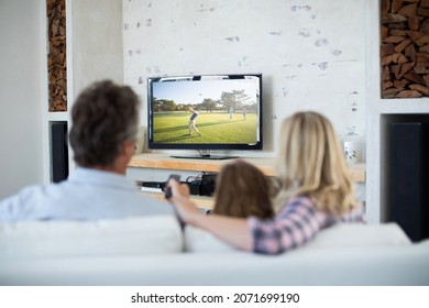 Rear View Of Family Sitting At Home Together Watching Golf Event On Tv. Sports, Competition, Entertainment And Technology Concept Digital Composite Image.