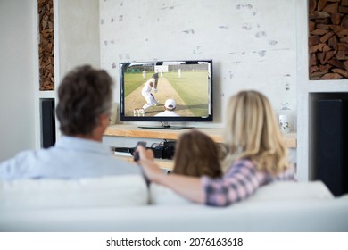 Rear View Of Family Sitting At Home Together Watching Cricket Match On Tv. Sports, Competition, Entertainment And Technology Concept Digital Composite Image.