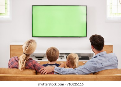 Rear View Of Family Sitting On Sofa In Lounge Watching Television