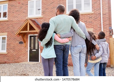 Rear View Of Family Standing Outside New Home On Moving Day Looking At House