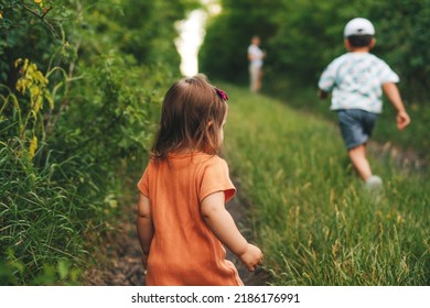 Rear View Of A Family Of Three Climbing A Green Hill To Reach Home In The Village, Returning From The Fields. Family Exploring Nature Together. Happy Family