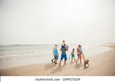 Rear View Of A Family Walking Along The Beach With Their Dog While On Holiday.