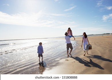 Rear View Of Family Walking Along Beach With Picnic Basket