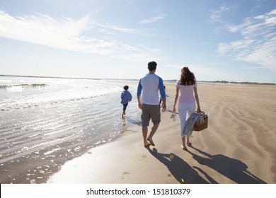 Rear View Of Family Walking Along Beach With Picnic Basket
