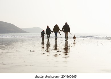 Rear View Of Family Walking Along Winter Beach With Dog