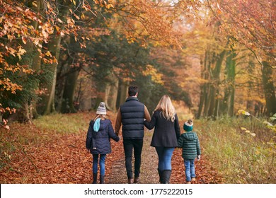 Rear View Of Family Walking Arm In Arm Along Autumn Woodland Path Together