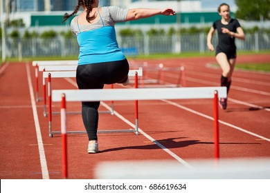 Rear View Of Fat Woman In Sportswear Running On Stadium And Overcoming Obstacles