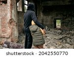 Rear view of father embracing child and looking at ruins of house after hostilities