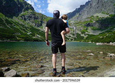Rear view at father holding kid son and looking at mountains view by the lake, Velicke mountain lake, Slovakia, High Tatras 